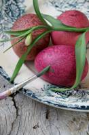 still life arrangement featuring purple-painted eggs with a sprig of leaves resting on them and a paintbrush at one side